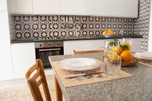 A kitchen with patterned backsplash, a dining table with plates and glasses, and a basket of oranges.