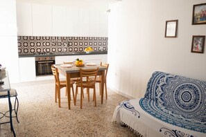 Un coin repas avec une table dressée pour quatre personnes, une cuisine en arrière-plan et un canapé à motifs.