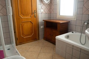 A bathroom with a wooden door, a bathtub, a wooden cabinet, and a window. - Melograno apartment (Loculi)