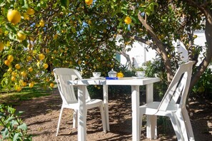 A white table and chairs set outdoors with a lemon tree in the background. - Melograno apartment (Loculi)
