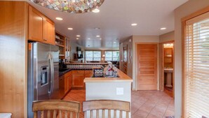 A spacious kitchen with wooden cabinets, a stainless steel refrigerator, a central island, and a mosaic ceiling light fixture. - Beachcomber Cottage · Close to Beach, Family Friendly, Open Layout (Pacific City)