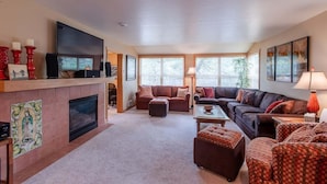 A spacious living room with a fireplace, two sofas, a coffee table, and a TV mounted on the wall. - Beachcomber Cottage · Close to Beach, Family Friendly, Open Layout (Pacific City)