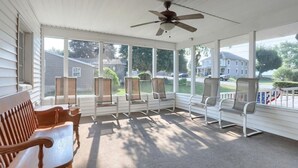 Eine überdachte Veranda mit Deckenventilator, mehreren Stühlen und einer Holzbank.