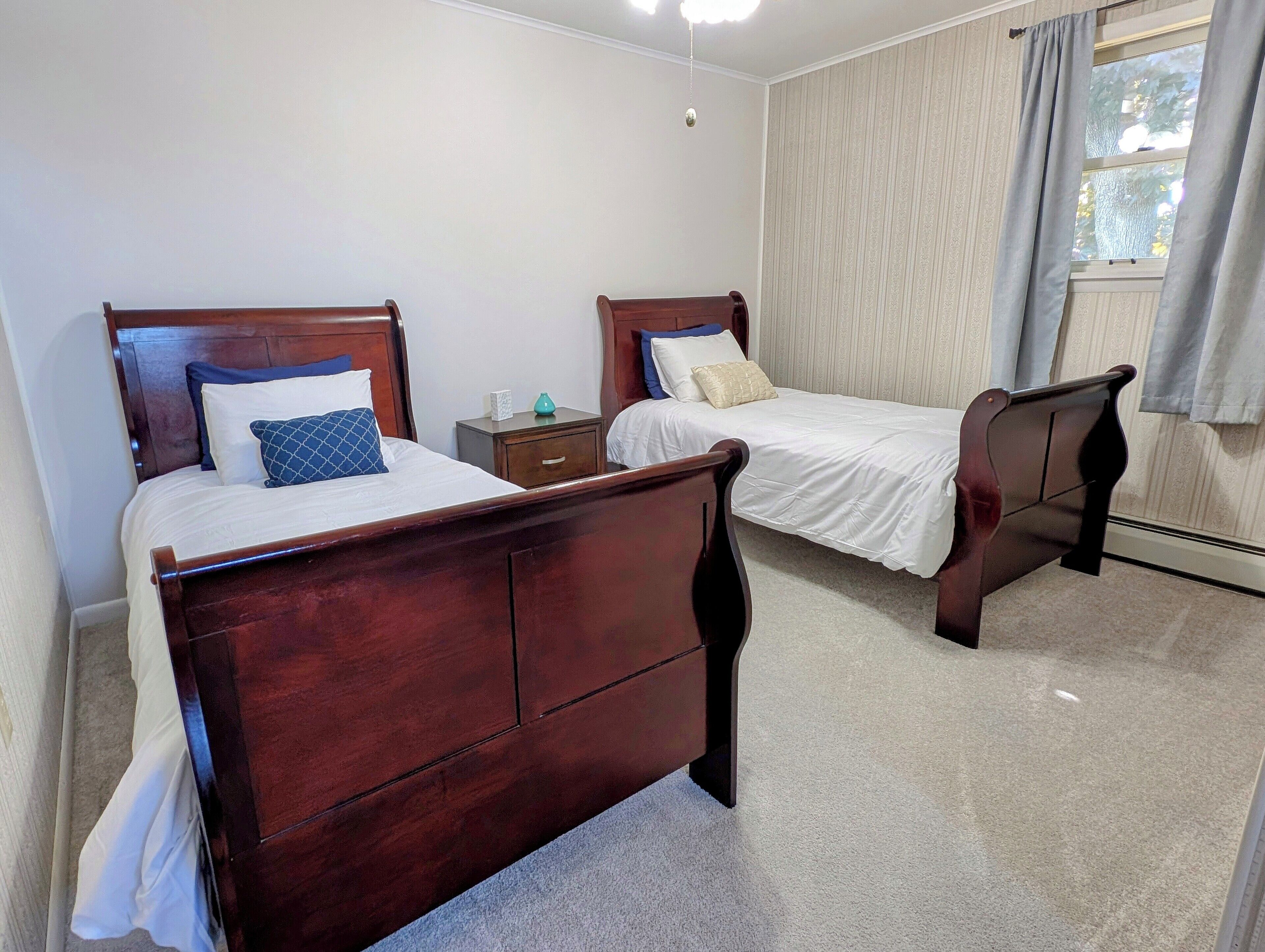 A bedroom with two wooden beds, a nightstand, a window with curtains, and a ceiling light.
