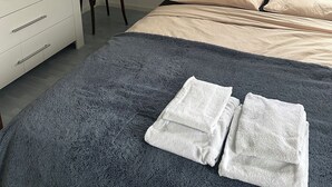 Une chambre à coucher avec un lit, une chaise, une commode et une fenêtre avec des rideaux.