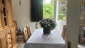 Un coin repas avec une table dressée pour quatre personnes, un buffet en bois et une fenêtre donnant sur un paysage verdoyant.