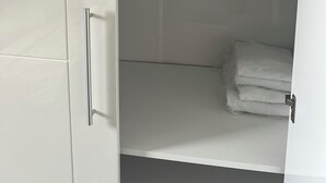 Une armoire blanche avec une porte de placard miroir et une étagère où sont pliées des serviettes.