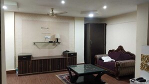 A living room with a sofa, a glass coffee table, a cabinet, a wardrobe, and a ceiling fan.