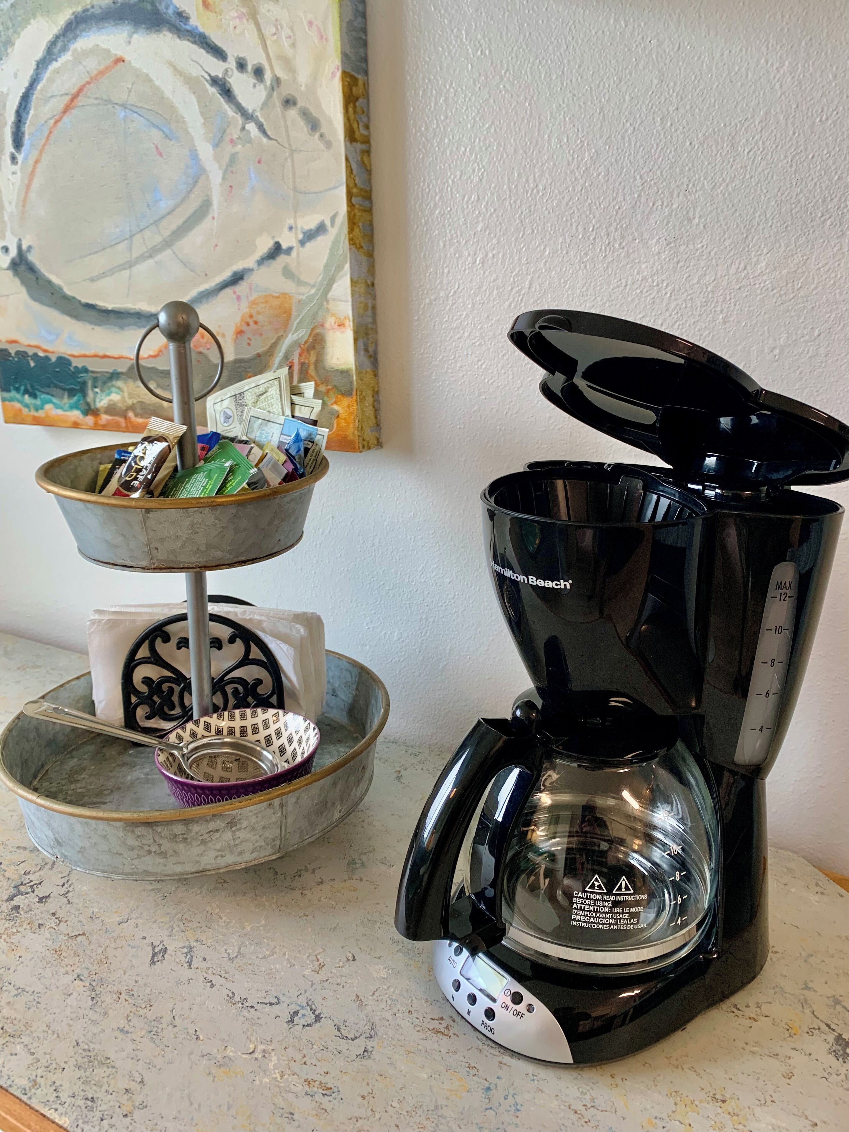 A coffee maker with a digital display and a scale, a metal container with a spoon and a strainer, and a decorative item with a pattern.