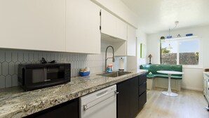 Eine moderne Küche mit einer Granit-Arbeitsplatte, einer schwarzen Mikrowelle und einer grünen Bank.