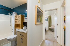 A bathroom with a shower, toilet, and sink, wooden cabinets, and a framed painting on the wall. - The Abode at 124°West -Ultra Comfortable and Stylish Arcata Retreat (Arcata)