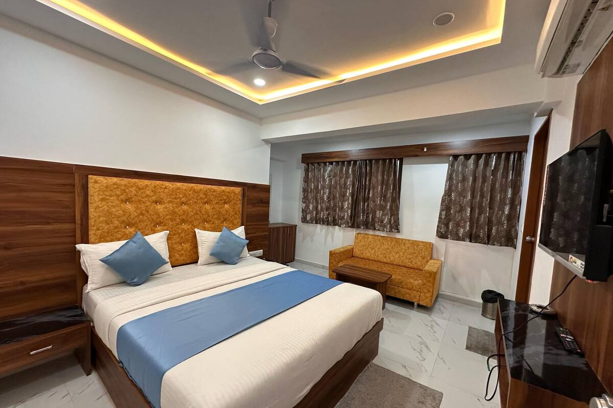A modern hotel room with a large bed, a sofa, a TV, and a ceiling fan.