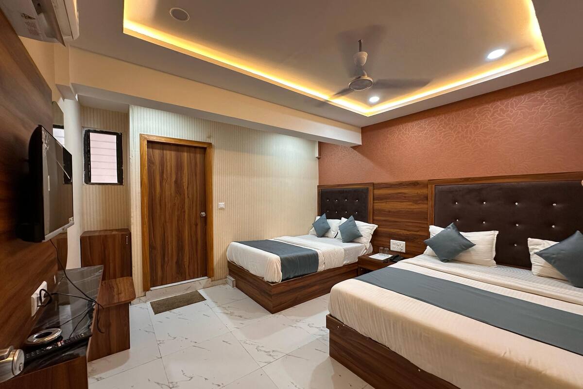 A hotel room with two beds, a TV, a wooden wardrobe, and a ceiling fan.
