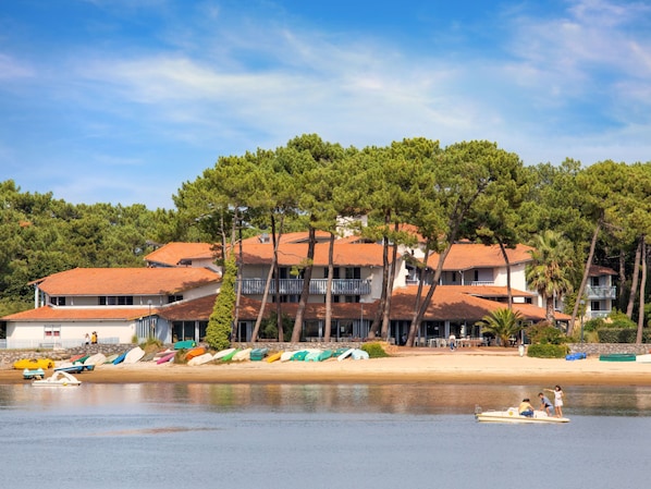 Un hotel frente al mar con varios balcones, una playa de arena y barcos.