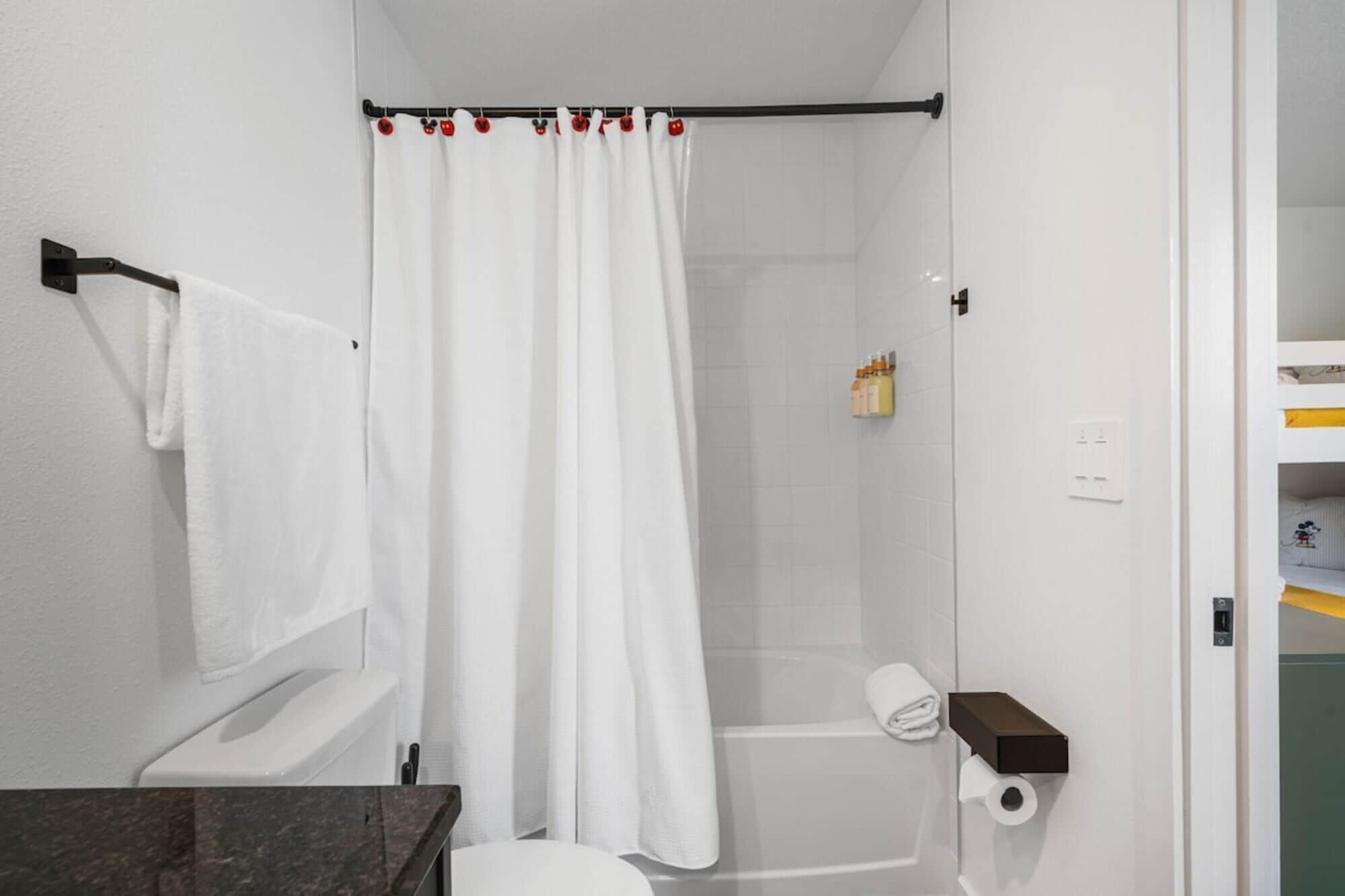 A bathroom with a shower curtain, a towel rack, a toilet, and a shelf with toiletries.