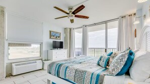 Une chambre à coucher avec un lit, un ventilateur de plafond, une télévision et une fenêtre avec des rideaux.