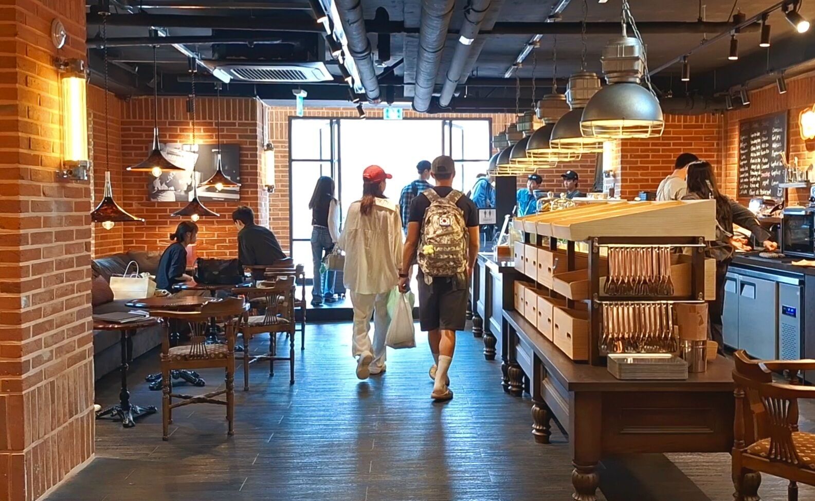 A restaurant interior with brick walls, hanging pendant lights, and a central walkway.
