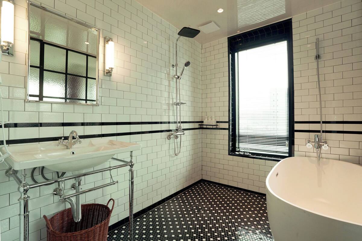 A bathroom with a white sink, a bathtub, a shower, and a window with blinds.