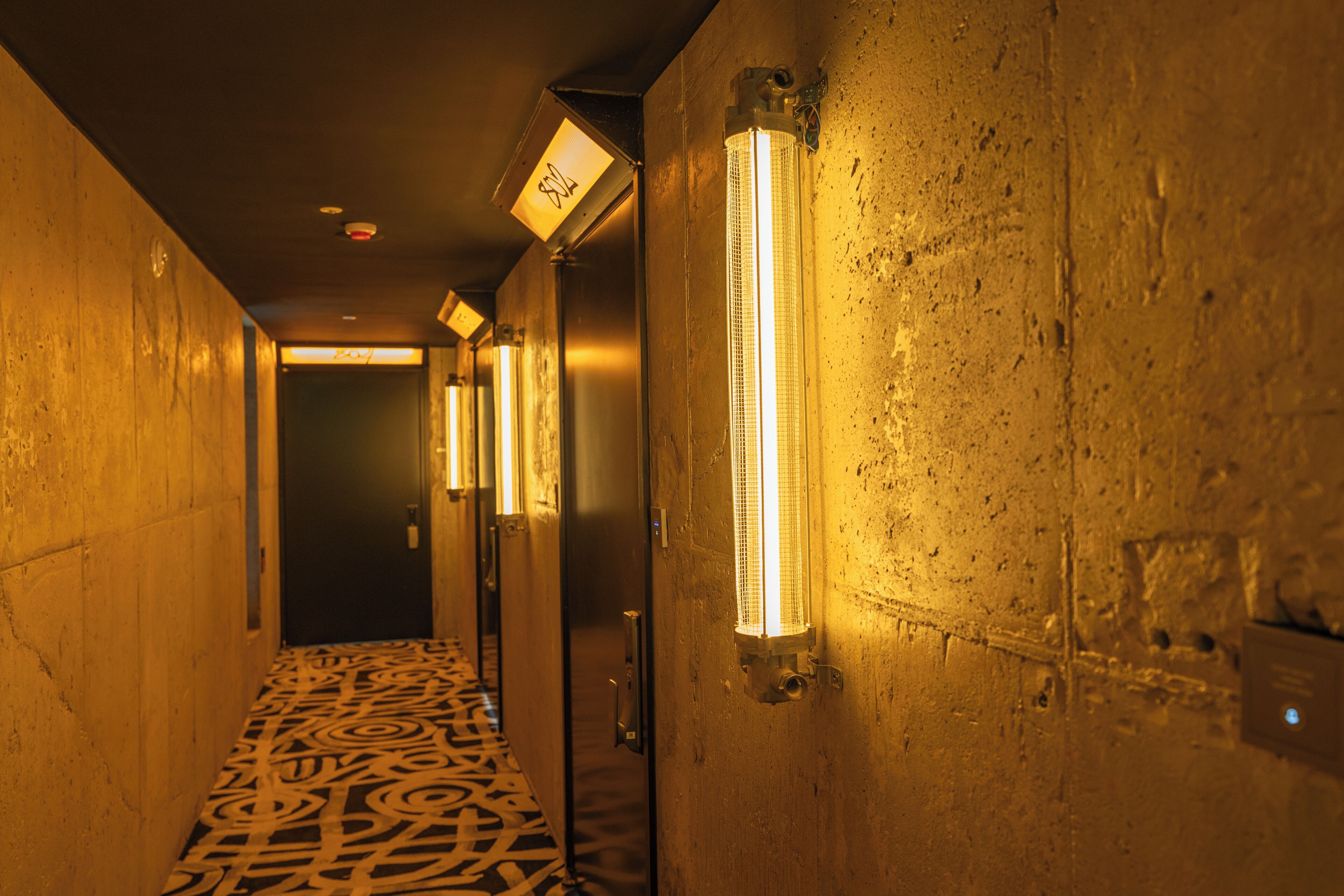 A hallway with patterned flooring, wall-mounted lights, and a door at the end.