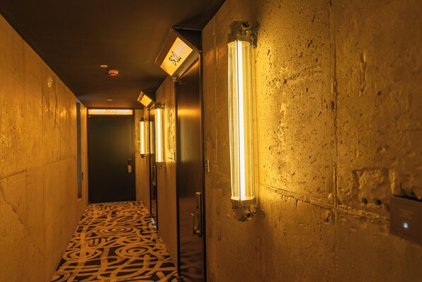 A hallway with patterned flooring, wall-mounted lights, and a door at the end. - Brooklyn Blues (Seoul)