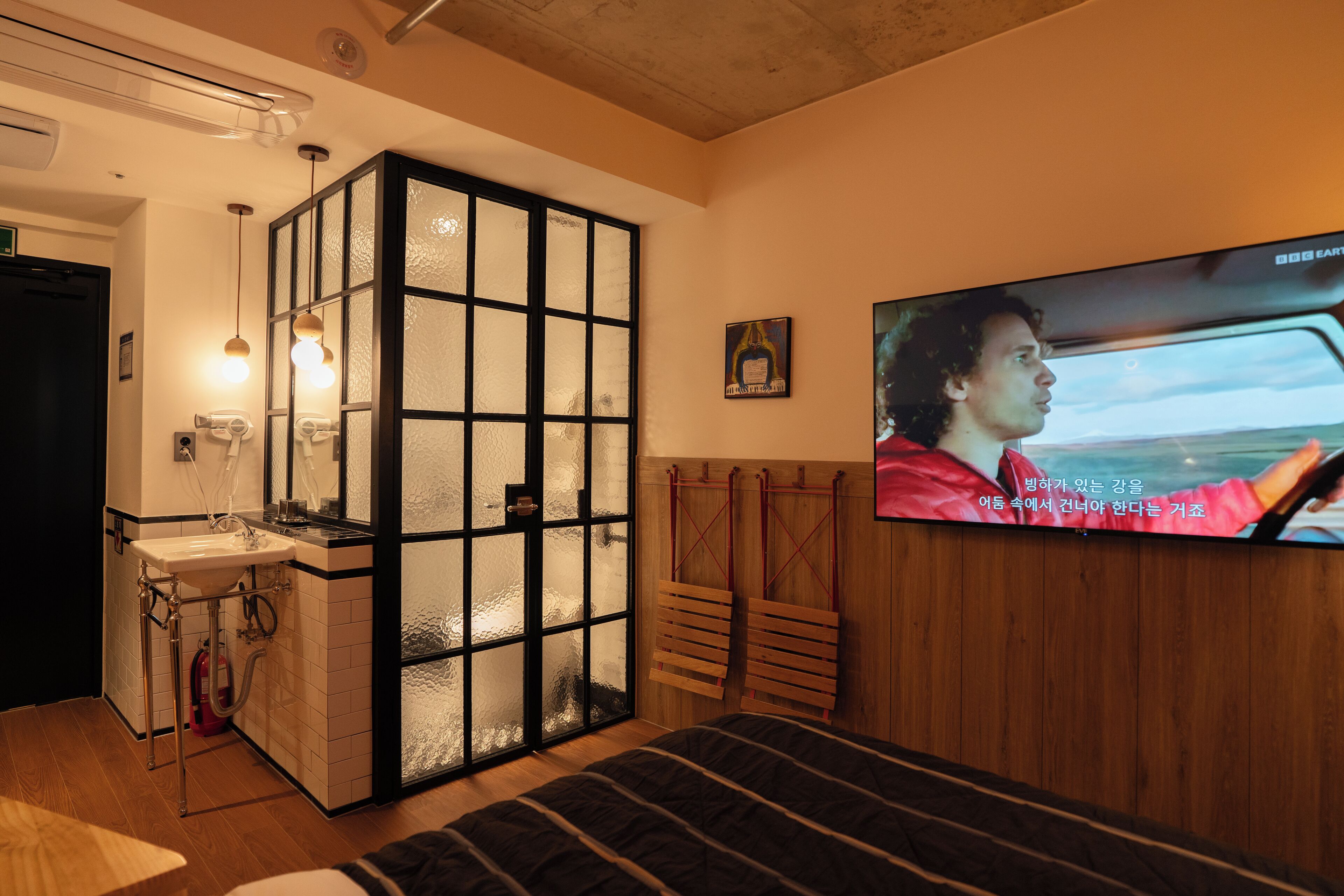 Ein Zimmer mit einem Bett, einem an der Wand befestigten Fernseher, einem Fenster mit Ausblick und einem kleinen Badebereich.
