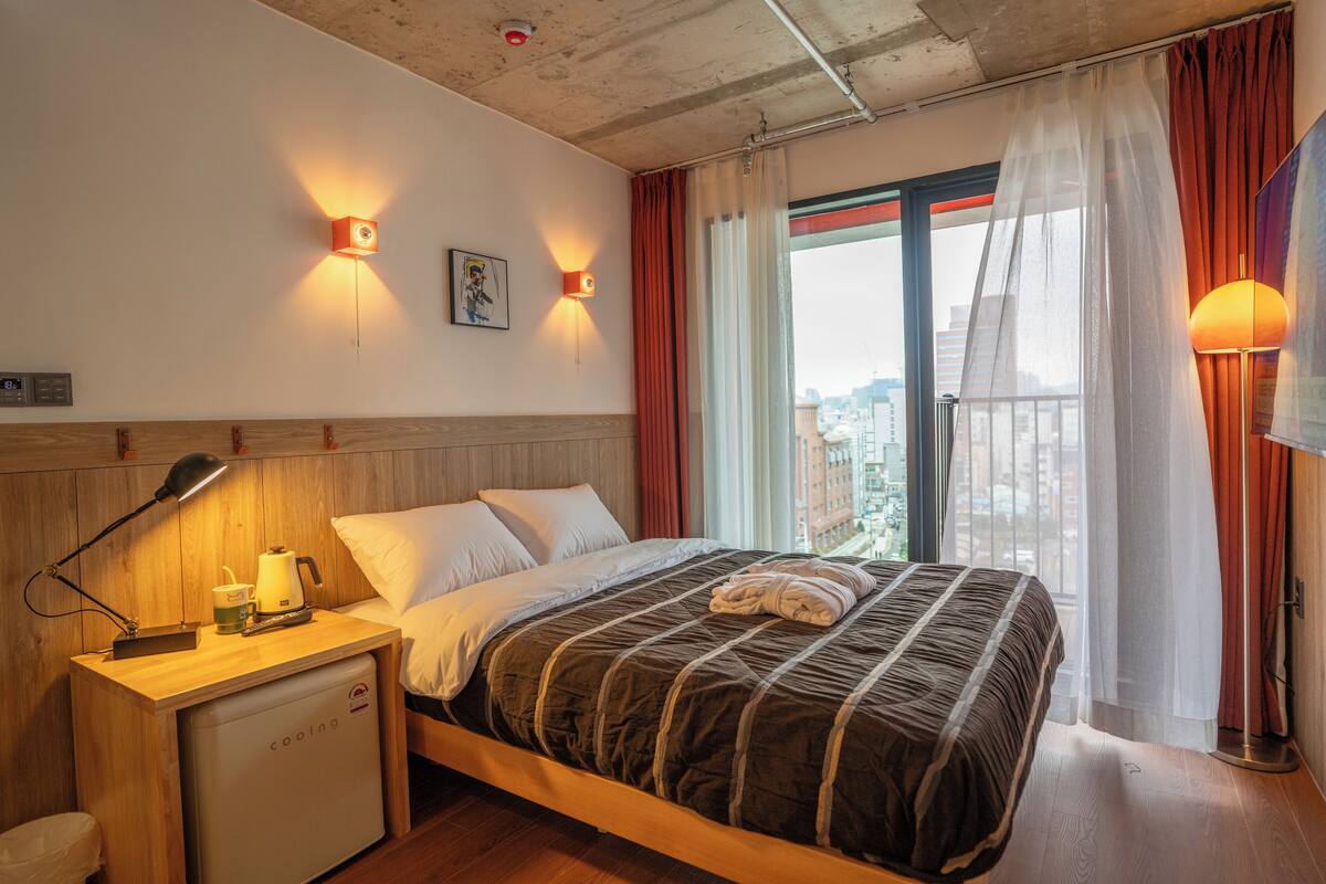 A hotel room with a bed, bedside table, lamp, and a small refrigerator.