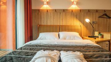 Una habitación de hotel con cabecera de madera, dos lámparas de noche, mesitas de noche de madera y una cama con ropa de cama blanca.