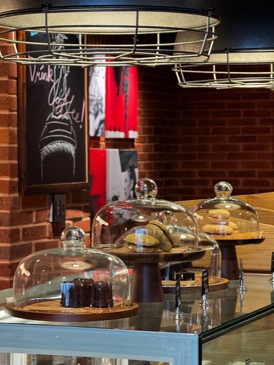 Une présentation de desserts sous des cloches de verre, avec un panneau en forme d’ardoise en arrière-plan.