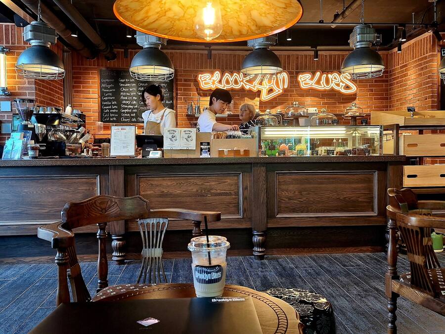 Acogedor interior de cafetería con pared de ladrillo, mostrador de madera y lámparas colgantes.