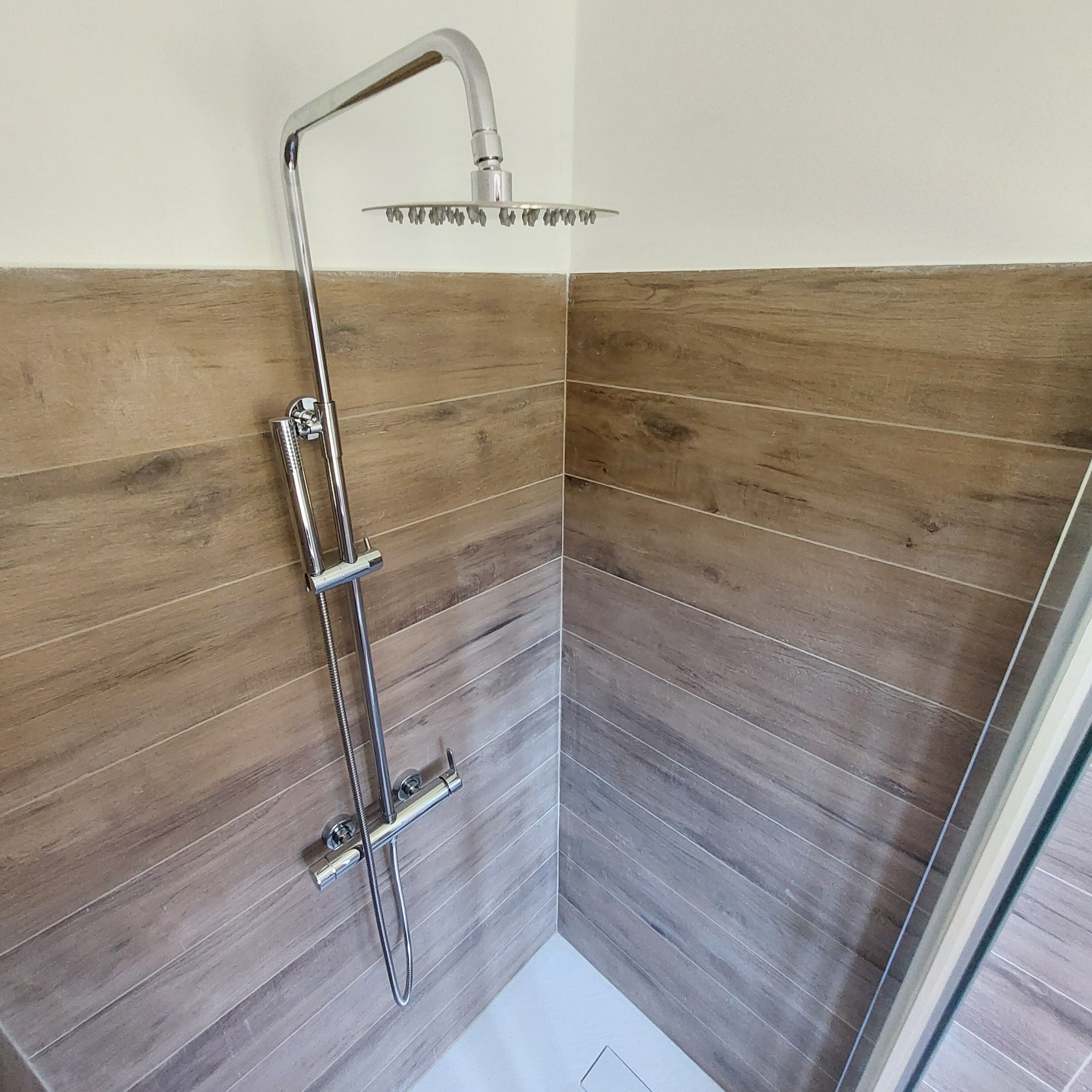 A shower with a handheld showerhead and a rain shower head, set in a corner with wooden panel walls.