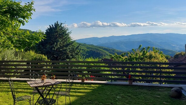 A patio with a table and chairs, surrounded by a wooden fence, overlooking a mountainous landscape.