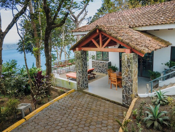 A covered outdoor seating area with stone pillars, a tiled roof, and a view of the sea.