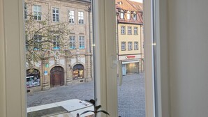 A room with a large window overlooking a cobblestone street and historic buildings. - Vacation apartment Olymp II, luxurious apartment in the heart of Bamberg (Bamberg)