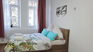 A bedroom with a bed, a window with curtains, a radiator, a wall-mounted light fixture, and a green chair. - Vacation apartment Olymp II, luxurious apartment in the heart of Bamberg (Bamberg)