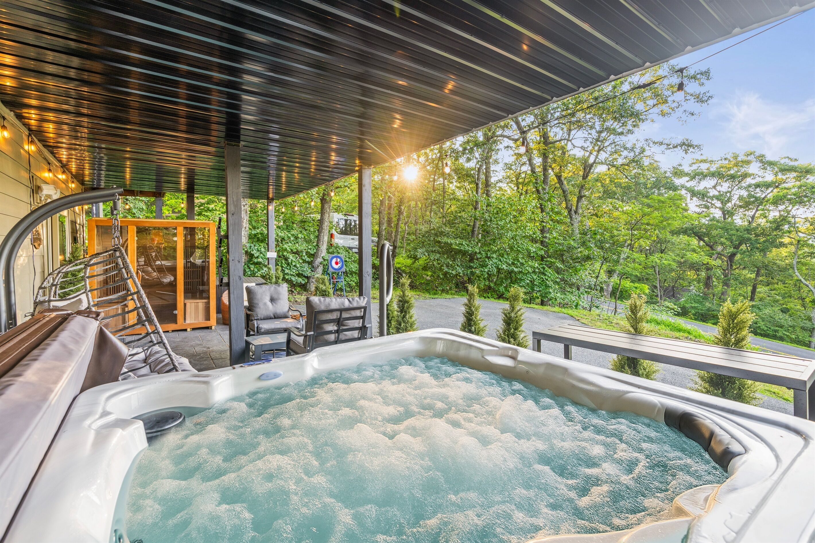 A hot tub with a view of a forested area, a covered patio with outdoor seating, and a glass door entrance.