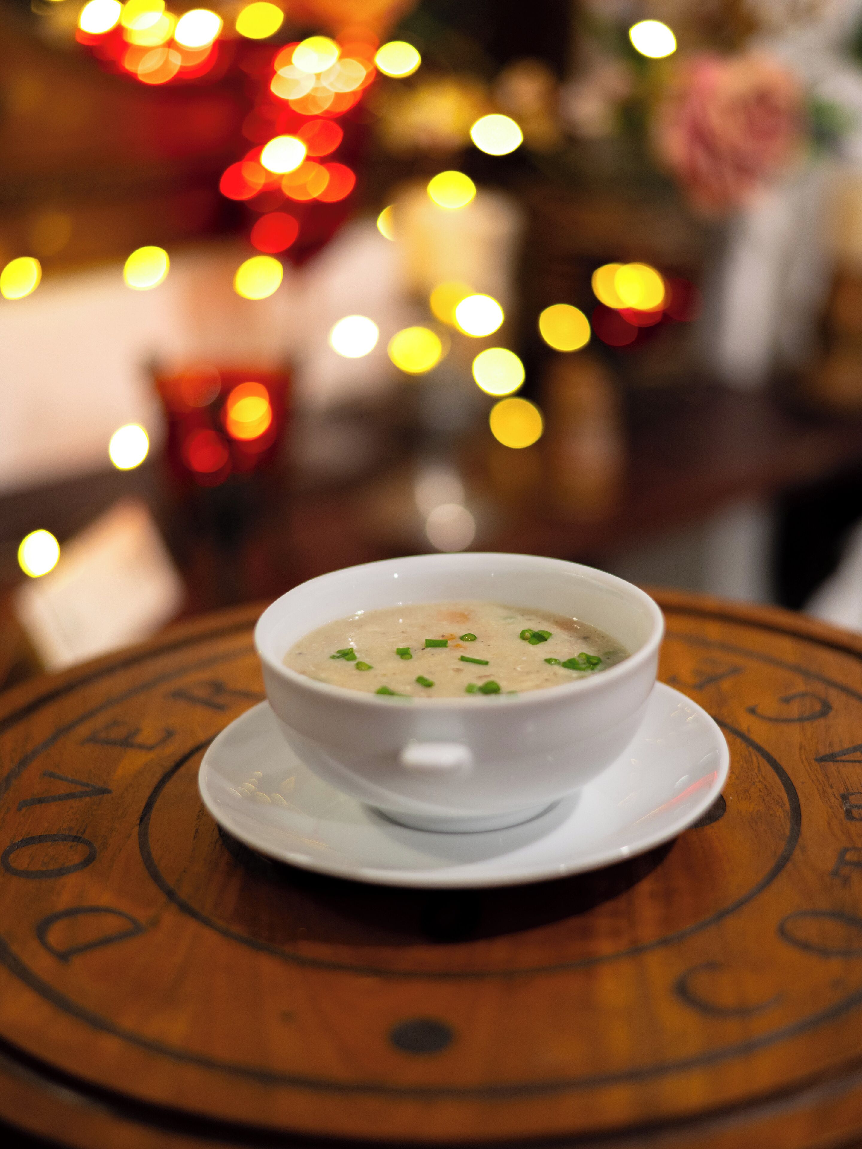 A bowl of soup on a wooden table with a decorative plate.