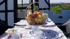 A table set for a meal with a fruit basket, plates, and cutlery, overlooking a scenic landscape. - Dover Cottage (Nuwara Eliya)