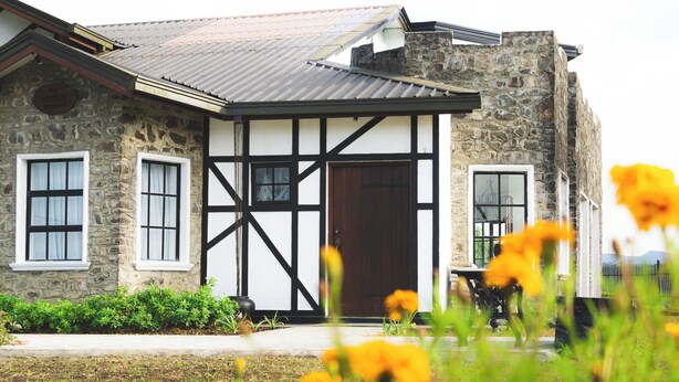 A stone building with a black and white exterior, a large wooden door, and a small porch. - Dover Cottage (Nuwara Eliya)