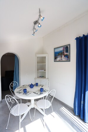 A dining area with a white table, four chairs, a white cabinet, and a painting on the wall.