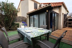A patio with a table set for four, surrounded by chairs, and a house in the background.