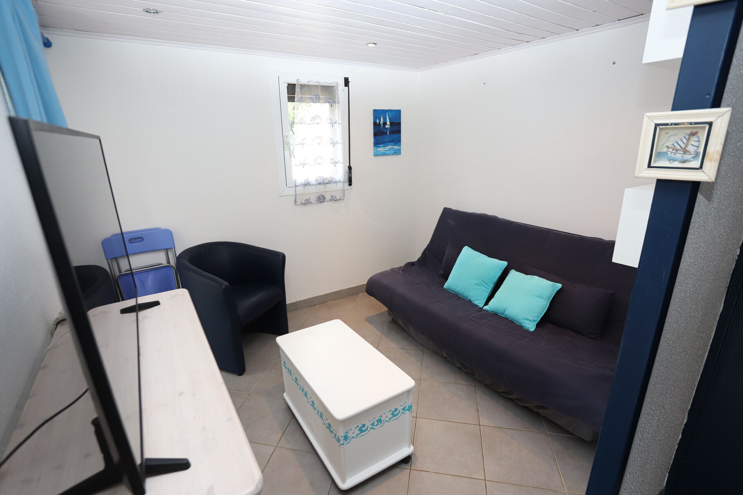A room with a desk, a chair, a sofa with blue cushions, a window with a curtain, and a framed picture on the wall.