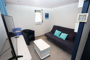 A room with a desk, a chair, a sofa with blue cushions, a window with a curtain, and a framed picture on the wall.