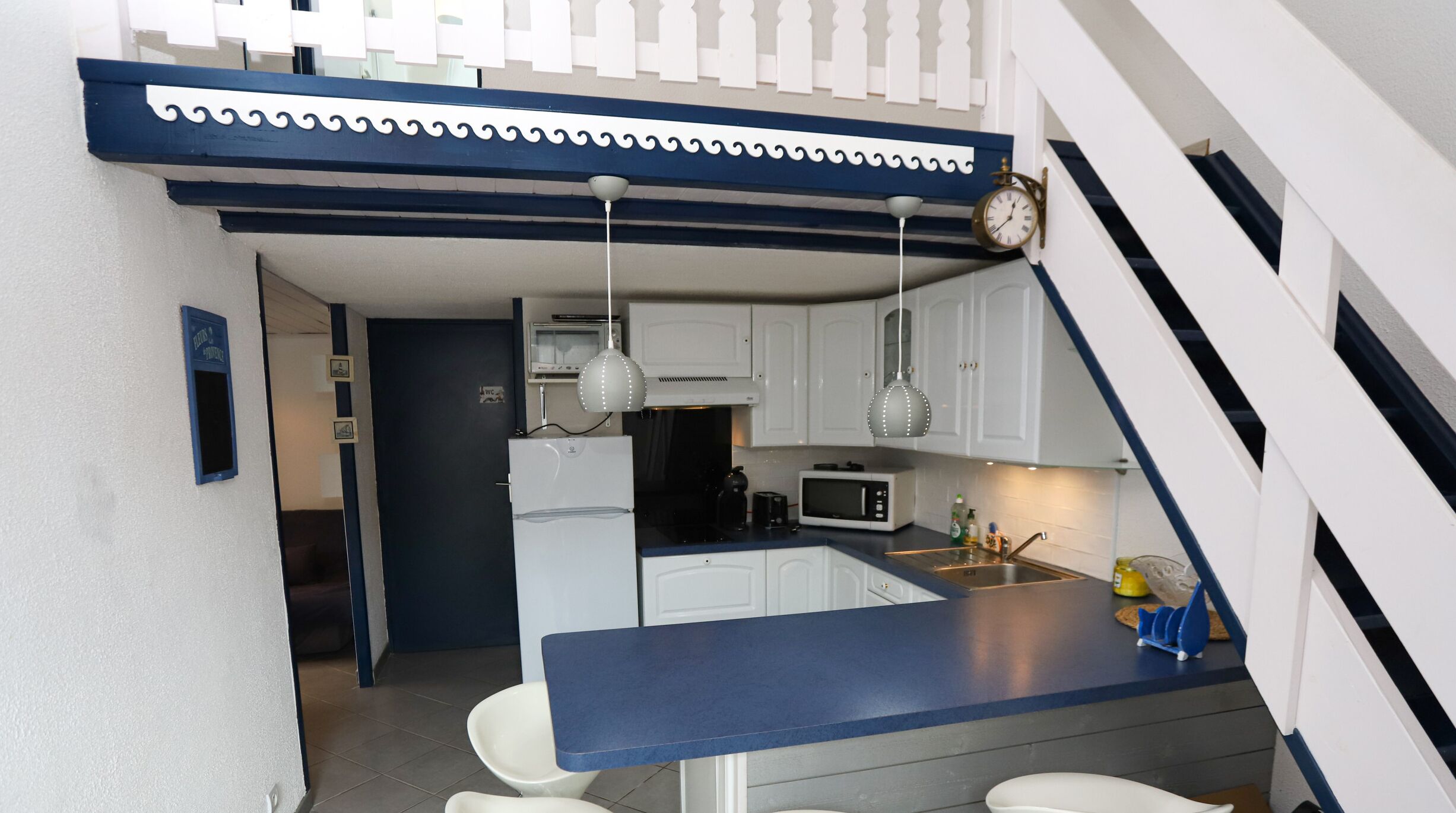 A compact kitchen with white cabinets, a blue countertop, and a clock on the wall.