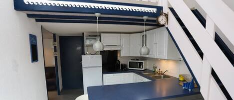 Una cocina compacta con armarios blancos, una encimera azul y un reloj en la pared.
