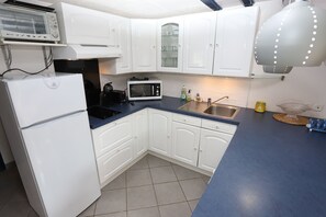 A kitchen with white cabinets, a microwave, a refrigerator, a sink, and a blue countertop.