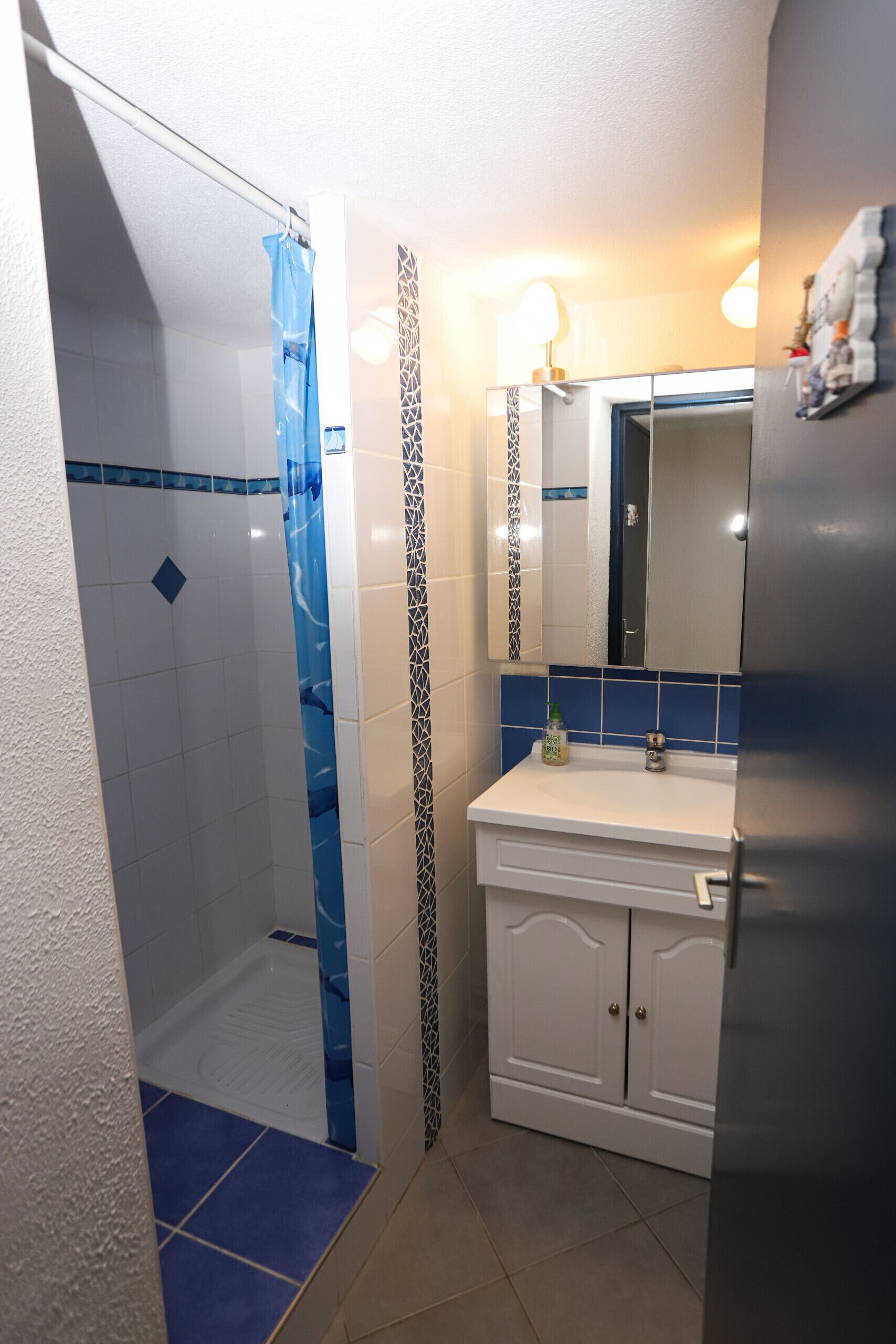 A bathroom with a shower, a sink, a mirror, and a cabinet.
