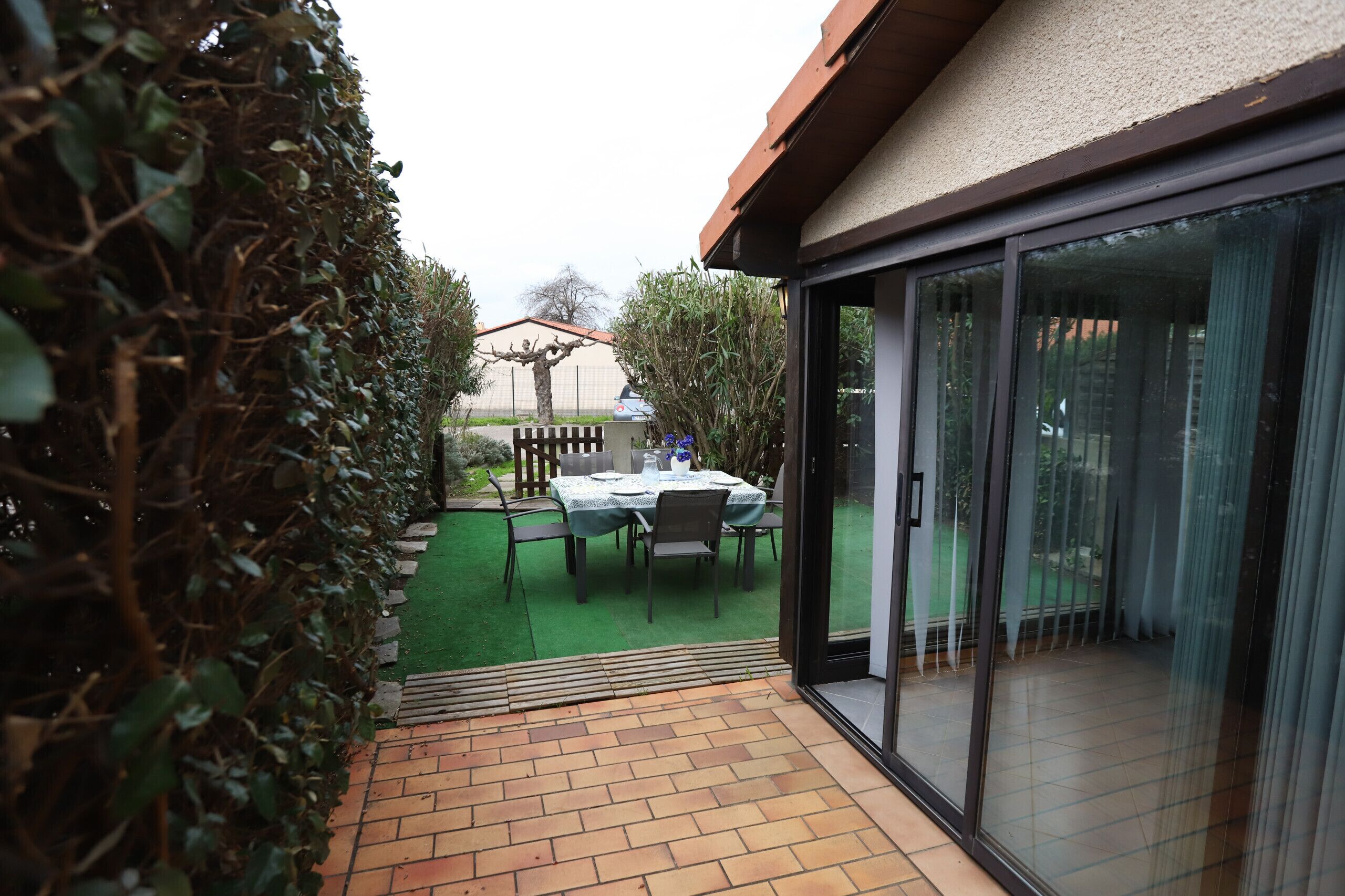 A patio area with a table and chairs, a brick floor, and a glass door leading to a covered outdoor space.