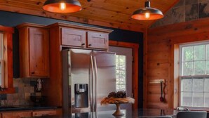A modern kitchen with wooden cabinets, a stainless steel refrigerator, and a central island with bar stools. - COZY Cabin with Hot Tub - Near all in Hocking Hills (Logan)