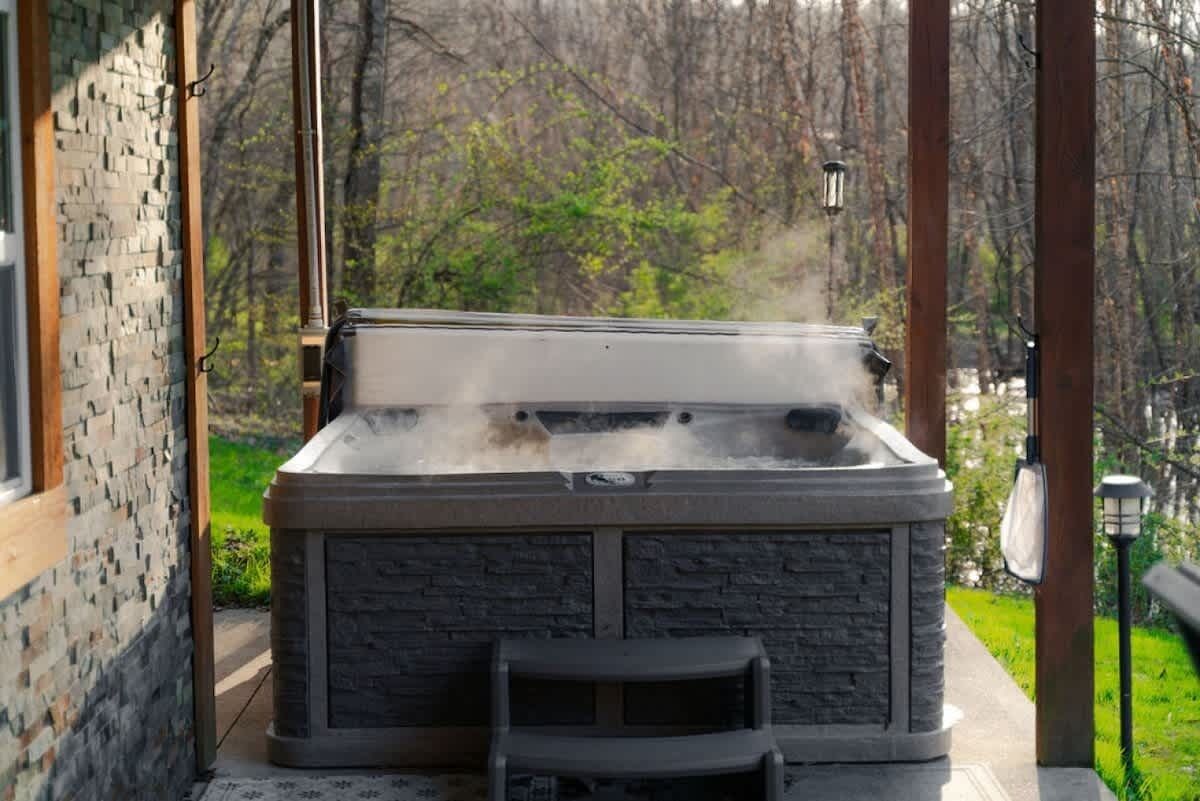 A hot tub with a stone exterior, a small seating area, and a view of a wooded area.