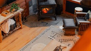 A cozy cabin interior with a stone fireplace, wooden furniture, and a view of the outdoors. - COZY Cabin with Hot Tub - Near all in Hocking Hills (Logan)